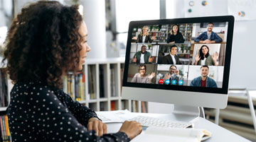 A woman at a desk with a computer screen displaying a video conference.